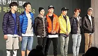 Seven men standing in line against a black wall