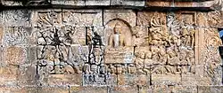 Buddha during the battle with Mara pointing towards the earth, summoning Phra Mae Thorani to come to his assistance from Borobudur. She is on the left hand and holding Kalasha.