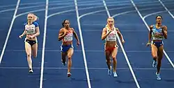 Photo of four athletes seen from the front while running on a blue athletics track