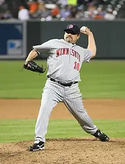 A man stands on the pitcher's mound in a gray baseball uniform with "Minnesota" written across the chest in red letters and a navy blue cap with a red "M" on the front about to throw a baseball.