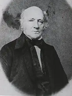 A black and white portrait photograph of a balding man in a suit