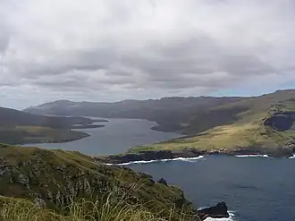 A narrow body of water between two grassy hills, with another body of water in the foreground separated by a small isthmus. The scene is dimly lit and overcast