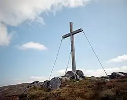 A color photograph of a white wooden cross erected upon a hilly landscape