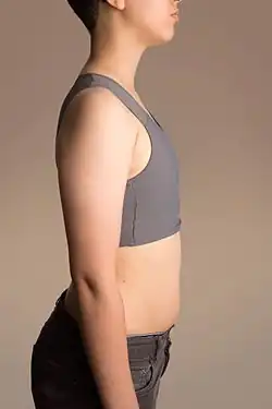 Partial profile view of a trans man wearing a grey binder