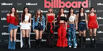 Members of Bini standing at Billboard Korea event, dressed in diverse and fashionable outfits in front of a branded backdrop