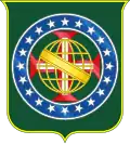 Coat of arms consisting of a shield with a green field with a golden armillary sphere superimposed on the red and white Cross of the Order of Christ, surrounded by a blue band with 20 silver stars; the bearers are two arms of a wreath, with a coffee branch on the left and a flowering tobacco branch on the right; and above the shield is an arched golden and jeweled crown.