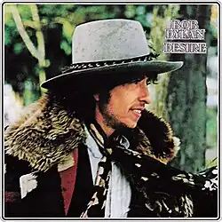 A profile of Dylan smiling, wearing a hat, coat, and scarves
