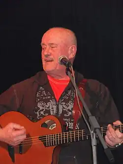 Petr Ulrych playing a guitar in front of a microphone, looking right of camera