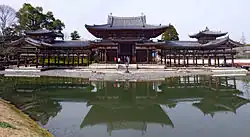 Wide wooden building on an island consisting of a central structure connected on either side to open corridors with towers at the end.