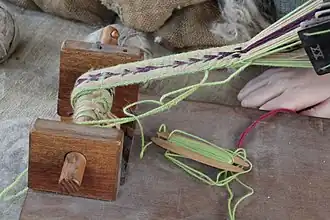 Belt or band shuttle, a short shuttle used for inkle weaving. This extra-sturdy shuttle is also used at a batten, to beat the newly woven weft against the previously woven fell.[31]
