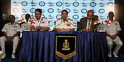 Uniformed man at a table, flanked by two other men