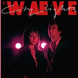 A photo of the duo stood side by side, bathed in red light and with two red spotlights behind them.