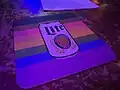 A coaster with the Philadelphia progress flag, with an image of Lite beer printed on it.