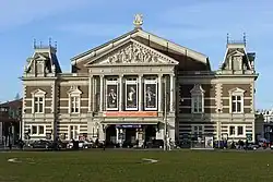 Photo of a symmetrical brick and stone building with a triangular pediment with a sculpted relief