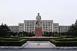 A photo of the Dalian University of Technology. A large statue of a famous Chinese person stands in the square of a sprawling university complex.
