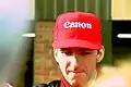 Damon Hill wearing a red baseball cap with sponsors logos signing autographs for fans