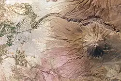 A mountain seen from above, next to green parks and cities
