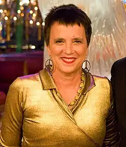 A woman in her late fifties sporting short hair and earrings with the nuclear disarmament logo.