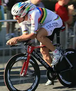 A cyclist wearing a rainbow skinsuit while riding a bike.