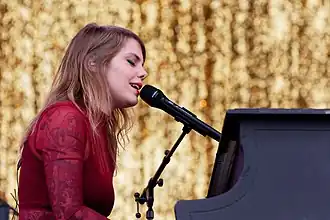 Béatrice Mireille Martin (Cœur de pirate) wearing a red dress, playing a piano and singing into a microphone onstage, with eyes closed