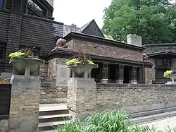 Exterior of Wright's studio as seen from Chicago Avenue. There is a low brick wall in front of the studio. Stairs lead through the brick wall, ascending to a terrace. There is a loggia with columns at the rear of the terrace. The main entrance is behind the loggia.