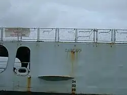 Close-up of a ship's light blue hull with the word "Cardiff" embossed on to it. There is rust drizzling down from the lettering.