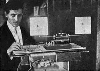 Spark oscillator similar to Hertz's, 1902. Visible are antenna consisting of 2 wires ending in metal plates (E), spark gap (D), induction coil (A), auto battery (B), and telegraph key (C).