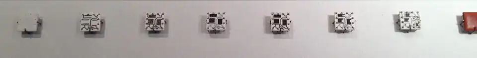 Steps in manufacturing Solid Logic Technology hybrid modules. The process starts with a blank ceramic wafer, 1⁄2 inch (13&nbsp;mm) square. Circuits are laid down first, followed by resistive material. Pins are added, the circuits are soldered and the resistors trimmed to the desired value. Then individual transistors and diodes are added and the package is encapsulated.