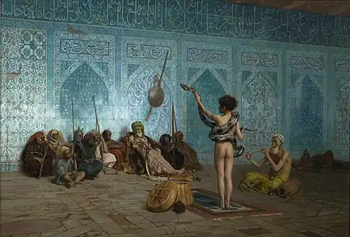 This painting shows the back side of a naked man standing with a snake wrapped around his waist and shoulders. The man is lifting up the head of the snake with his left hand. Another man to his right is sitting on the ground playing a pipe. A group of 10 men are sitting on the floor facing the snake handler with their backs against an ornate blue mosaic wall decorated with Arabic calligraphy.