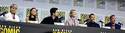 Linda Hamilton, Natalia Reyes, Diego Boneta, Mackenzie Davis, Gabriel Luna and Arnold Schwarzenegger seated at a table on a dais.