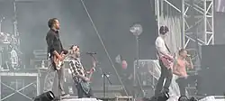 A color photograph of members of the group Linkin Park performing on and outdoor stage