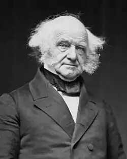 Half-length photographic portrait of an elderly, balding man dressed in a dark coat, vest and cravat