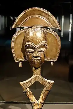 Mbulu viti reliquary figure; 19th-20th century; wood, brass, copper; by Kota people; Ethnographical Museum of Berlin. Finely carved and overlaid with contrasting cooper and brass, this sculpture combines shimmering surfaces, minimal depiction of physical features and body, and an imaginative elaboration of the head