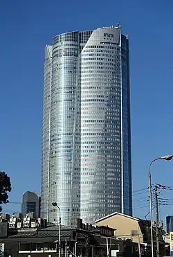 Aerial view of a gray, oval-shaped high-rise lined with rows of windows; the facade is bisected by a smaller midsection