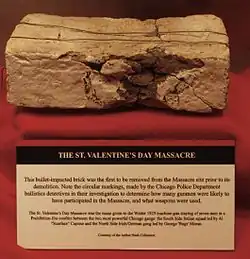 A brick with the following notice: "This bullet-impacted brick was the first to be removed from the Massacre site prior to its demolition. Note the circular markings, made by the Chicago Police Department ballistics detectives in their investigations to determine how many gunmen were likely to have participated in the Massacre, and what weapons were used."