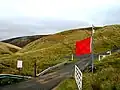 Otterburn Ranges. The road leading into the Ministry of Defence Ranges, and the red flag showing that the army are practising live firing there.