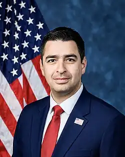 Official House portrait of Evans smiling in front of the U.S. flag, wearing a black suit with American flag lapel pin with the text "Veteran", white shirt, and red tie.