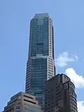 Ground-level view of 70-storey building. The exterior has a reddish hue with dark windows. The building tapers slightly at two points.