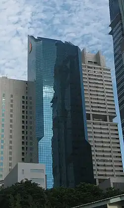 Distant ground-level view of a 40-story building with a blue glass facade; the building has a rectangular cross-section and a diagonal roofline.