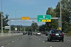 A four-lane freeway separated from oncoming traffic by a concrete barrier. A sign in the background indicates that the exit for State Route 202 is approaching.
