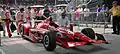 A red racing car adorned with sponsors logos on pit road is being pushed back into the garage