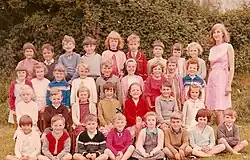 Group of children seated in rows next to a standing woman.