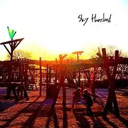 A photograph of a playground, including two children sat next to each other on a swingset, with the sun low in the sky in the background.