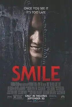 The zipper of a partially open bodybag reveals the face of a woman with a rictus grin