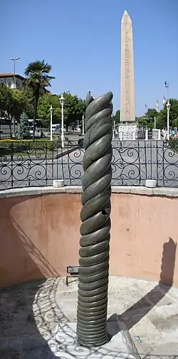 Photograph of a column damaged at the top, displayed in a public square