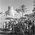 Tourists pose for a photo with locals in front of the castle. 1950s.
