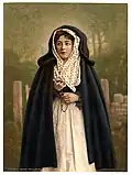 An 'Irish Colleen' wearing a cloak and holding rosary beads