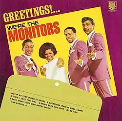 A photo of the band looking to the camera, smiling in suits and a white dress resting on a table, with a manila envelope overlapping it that lists the tracks