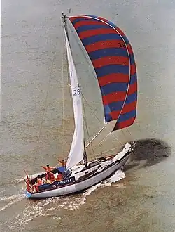 A single-masted yacht under sail, with crew on deck and waving.