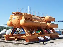 A structure of several dome-ended yellow steel cylinders standing on two full-length skids on a concrete slab.